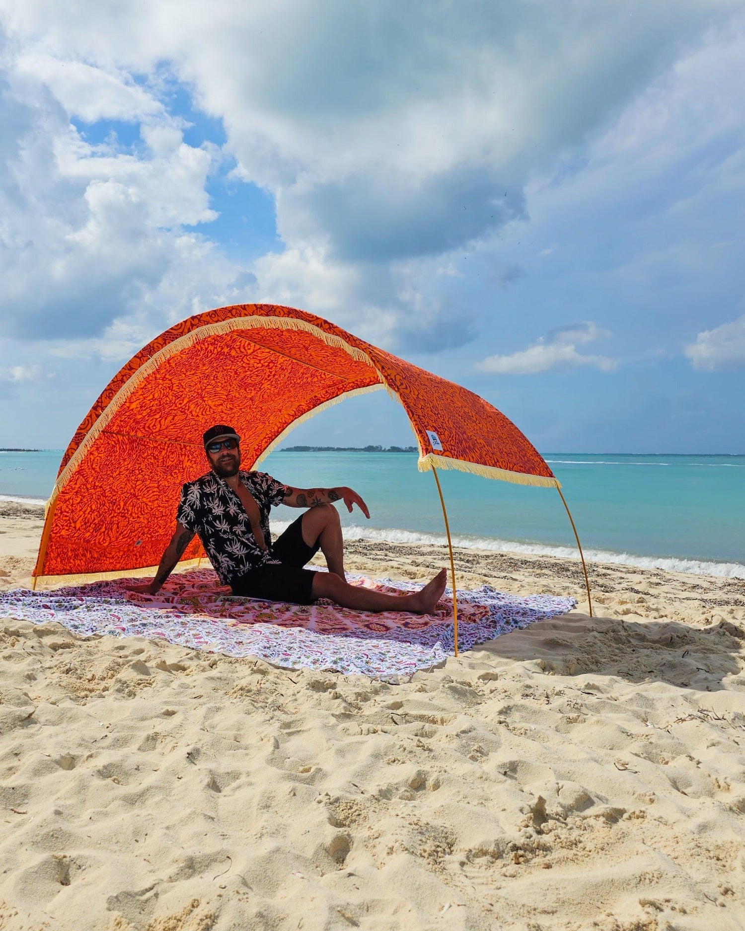 Suniela Tribal Jungle beach cabana with adjustable canopy pulled to one side for targeted sun protection, set up on the sand with a person relaxing underneath.