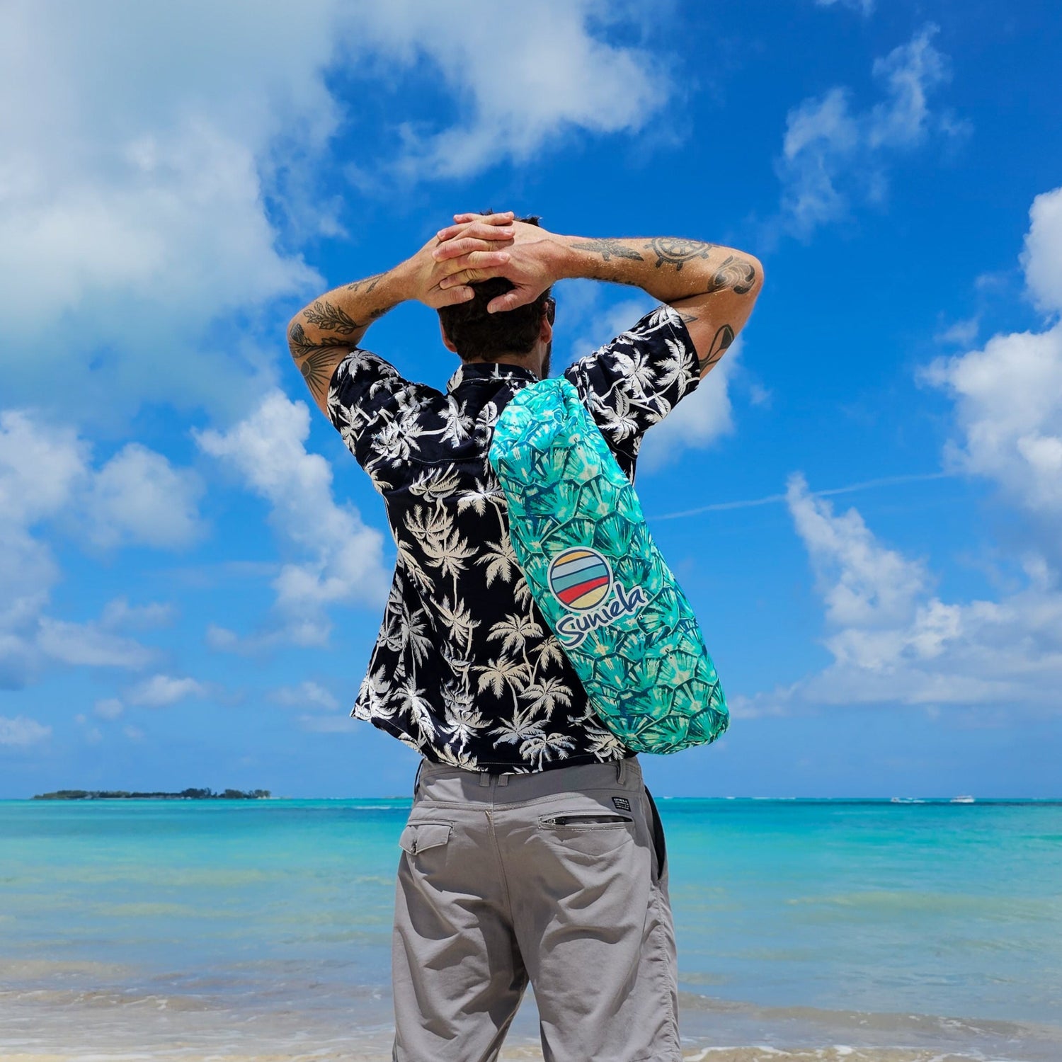 Man standing at the shoreline with a Suniela Tortoise Shell cabana slung over his shoulder, hands resting behind his head as he looks out at the ocean.