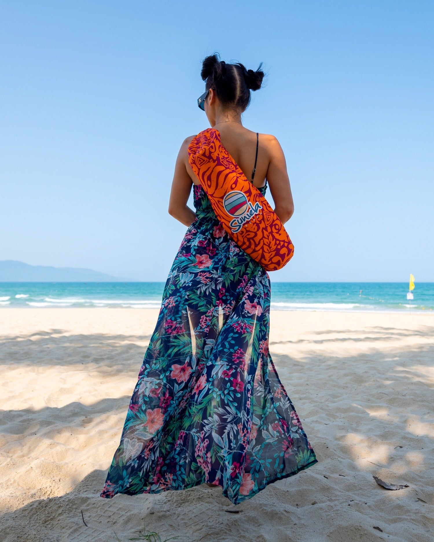 Woman standing on the beach wearing a Suniela Tribal Jungle cabana bag over her shoulder, highlighting the compact and lightweight design