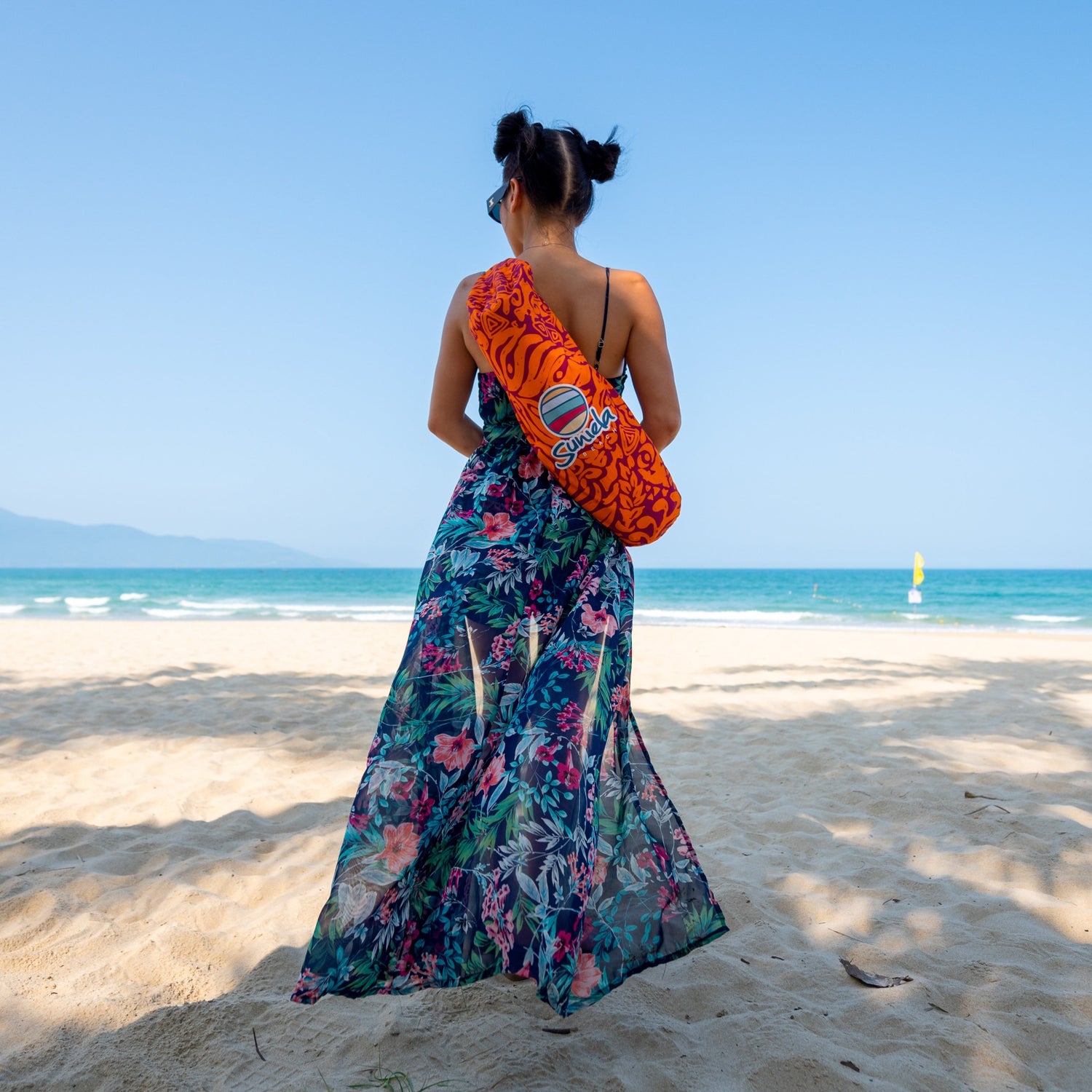 Woman standing on the beach wearing a Suniela Tribal Jungle cabana bag over her shoulder, highlighting the compact and lightweight design
