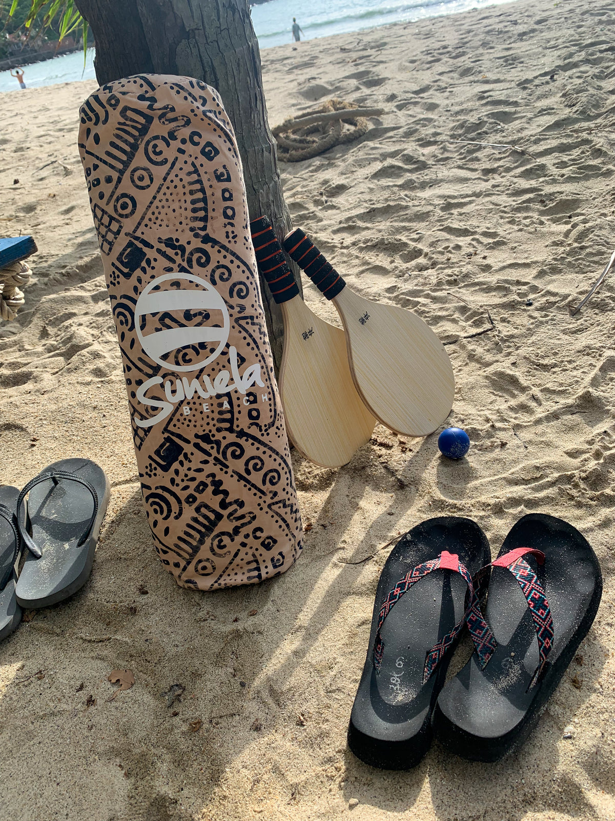 A beach scene with flip flops and a Tan coloured Suniela Beach shade cabana next to a paddleball game