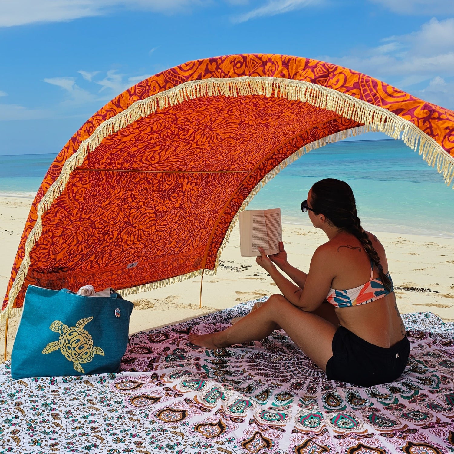 Woman reading beneath a Suniela beach cabana featuring the Tribal Jungle cotton canopy with decorative fringe
