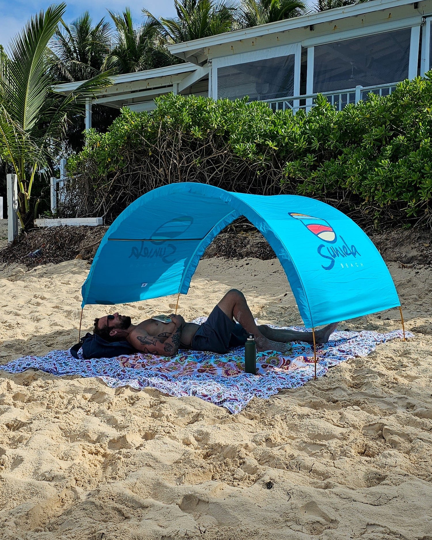 Man relaxing under a turquoise Suniela portable beach cabana on a sandy beach