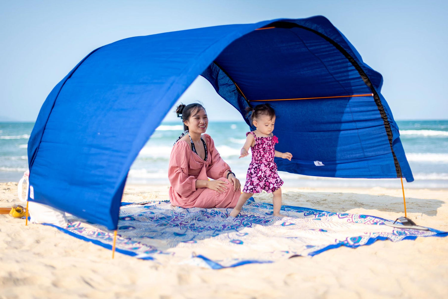 Mom and toddler play in the shade beneath their arched Suniela Beach shade tent