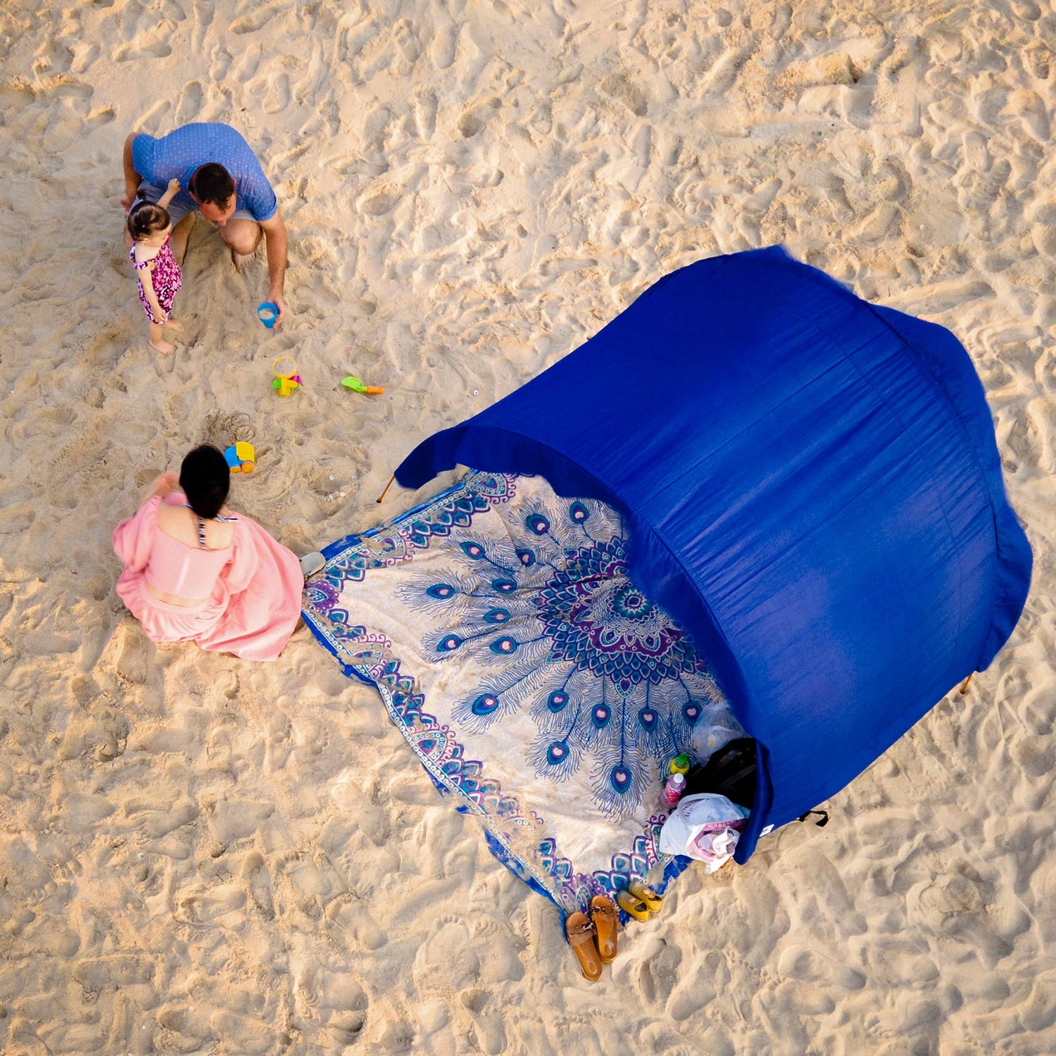 Family playing in the sand near their blue Suniela shade cabana.  Arched beach tent with beautiful cotton mat underneath