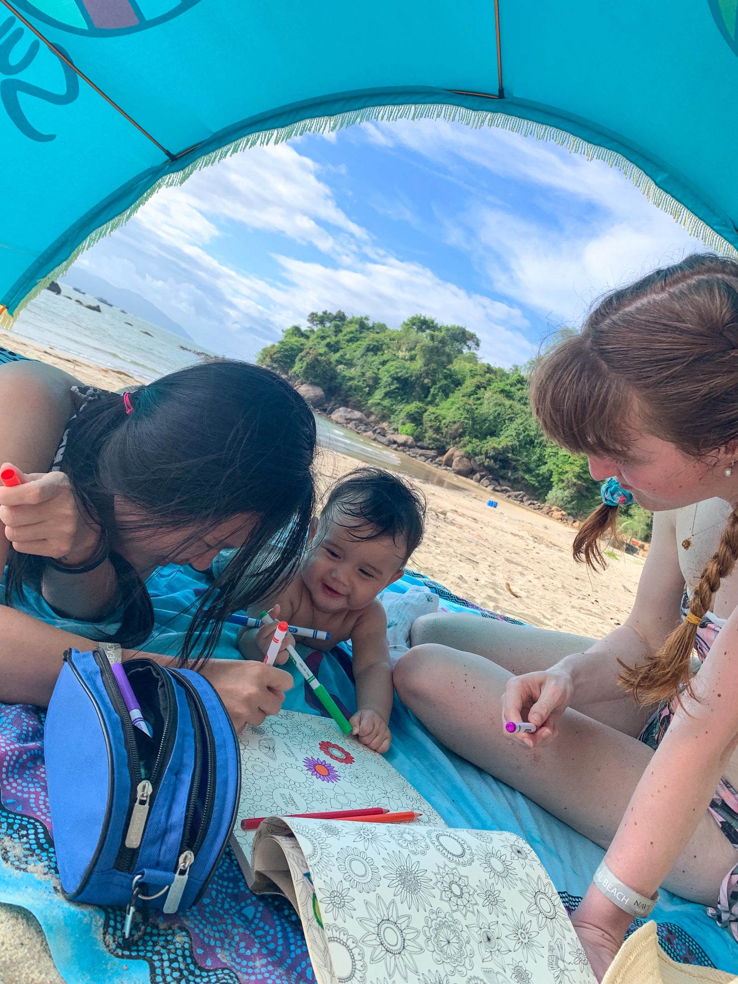 Baby and family colouring in the shade beneath their Turquoise Suniela beach cabana