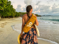 A woman walks on the beach carrying a yellow and green patterned Suniela shade cabana over her shoulder.