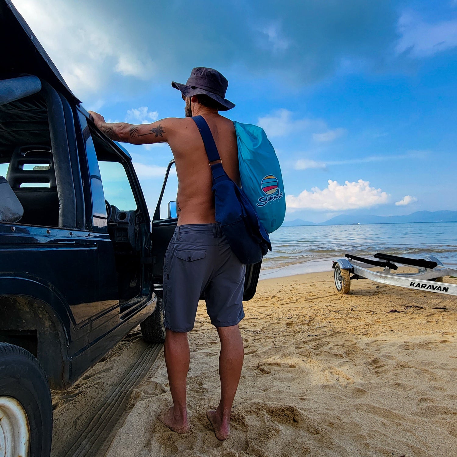 Man standing by a Jeep on a sandy beach carrying a Suniela portable beach cabana in its compact carry bag
