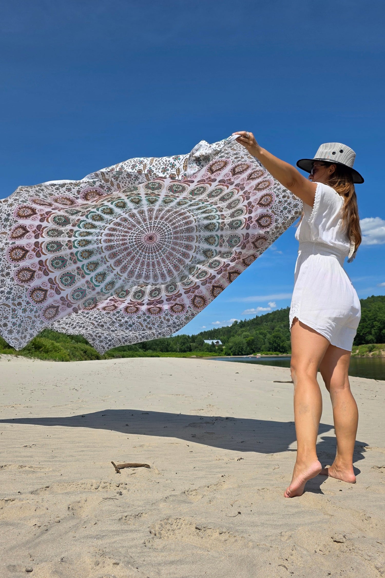 A woman holds a large printed beach mat in the breeze before laying it down on the sand.