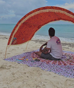 man removes his shirt and places it in the mesh pocket of his Suniela shade cabana, along with many other items before relaxing and looking out to the ocean