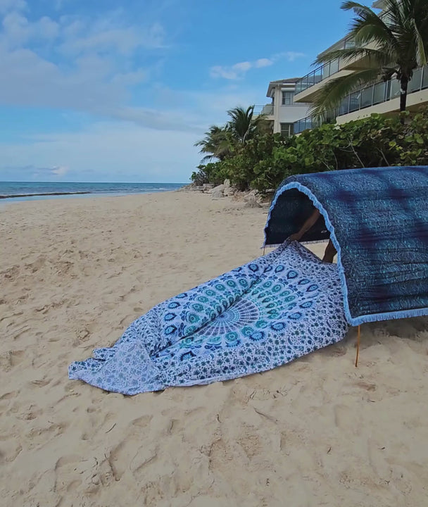 video of a woman laying out a large mandala beach mat under a blue Suniela shade cabana on a tropical beach
