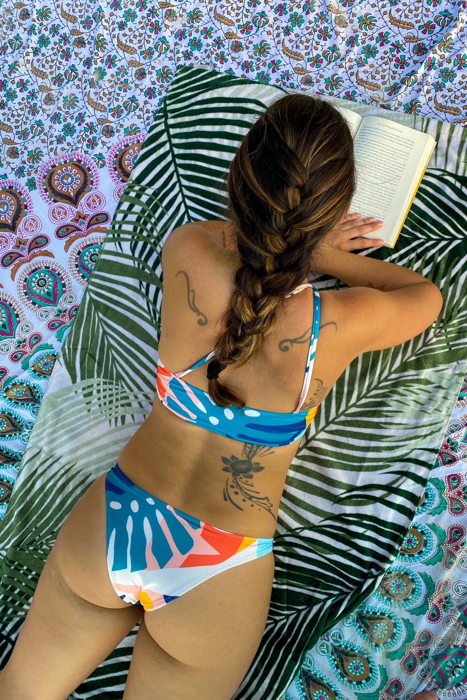 A woman in a bikini lies on a cotton beach mat, printed in traditional mandala design