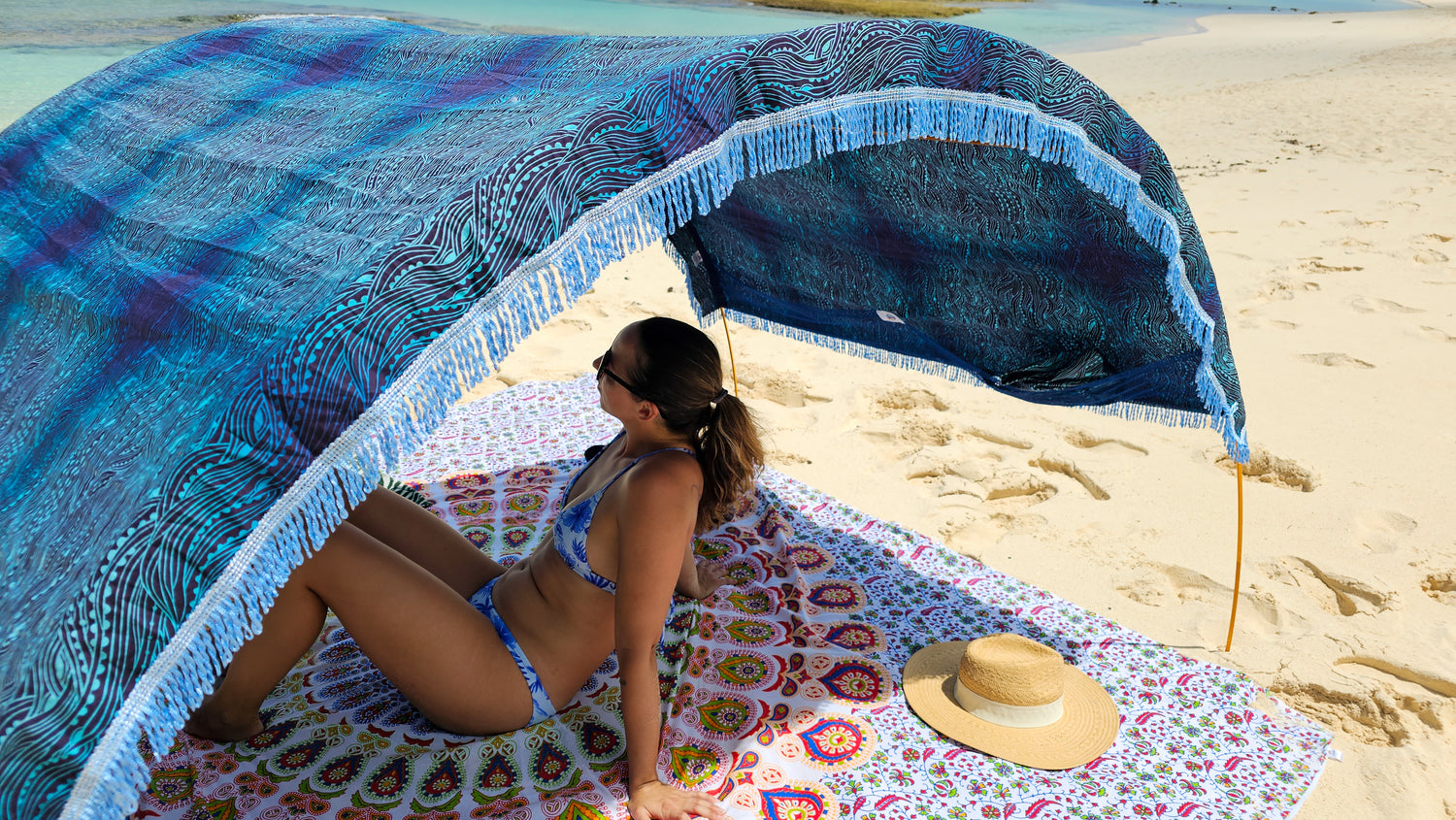 Woman relaxes on a large Suniela cotton beach mat beneath her blue shade canopy