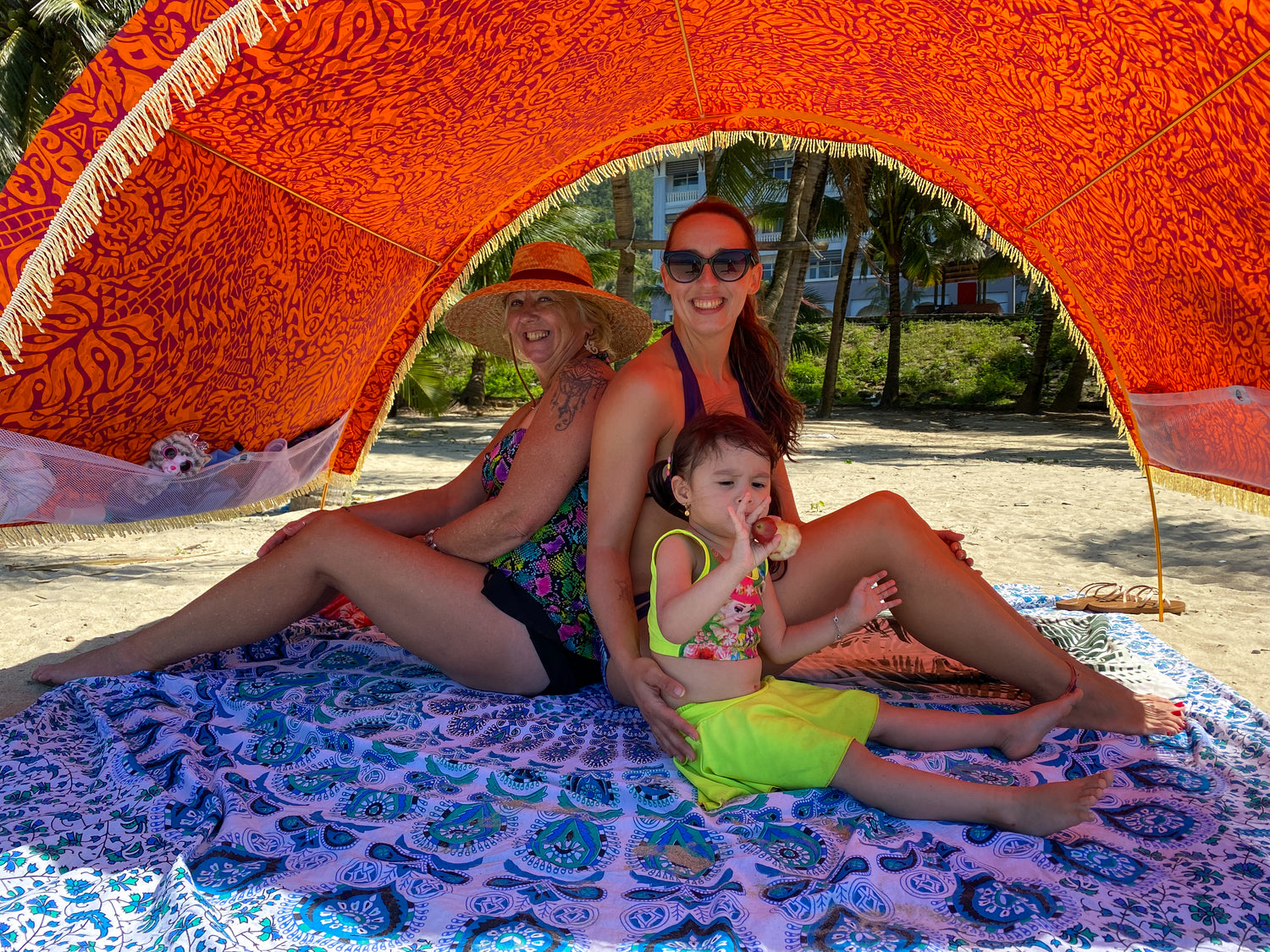 family with little girl sits on a blue cotton beach mat by Suniela