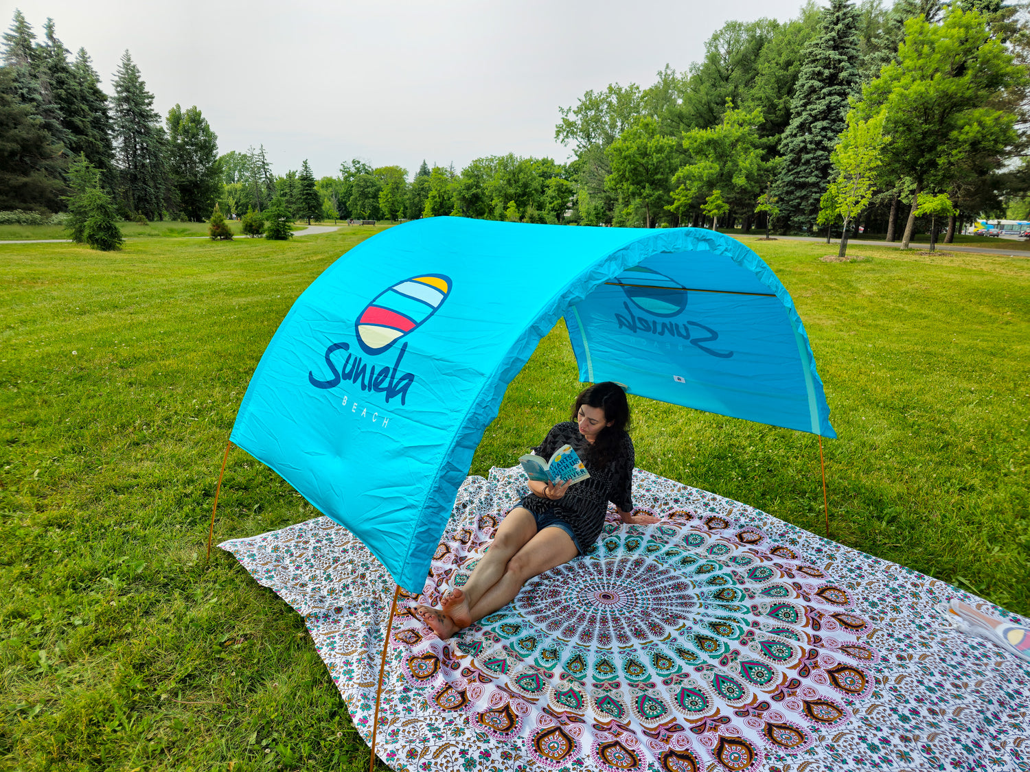 woman reading a book in the park while sitting on a giant cotton blanket by Suniela Beach